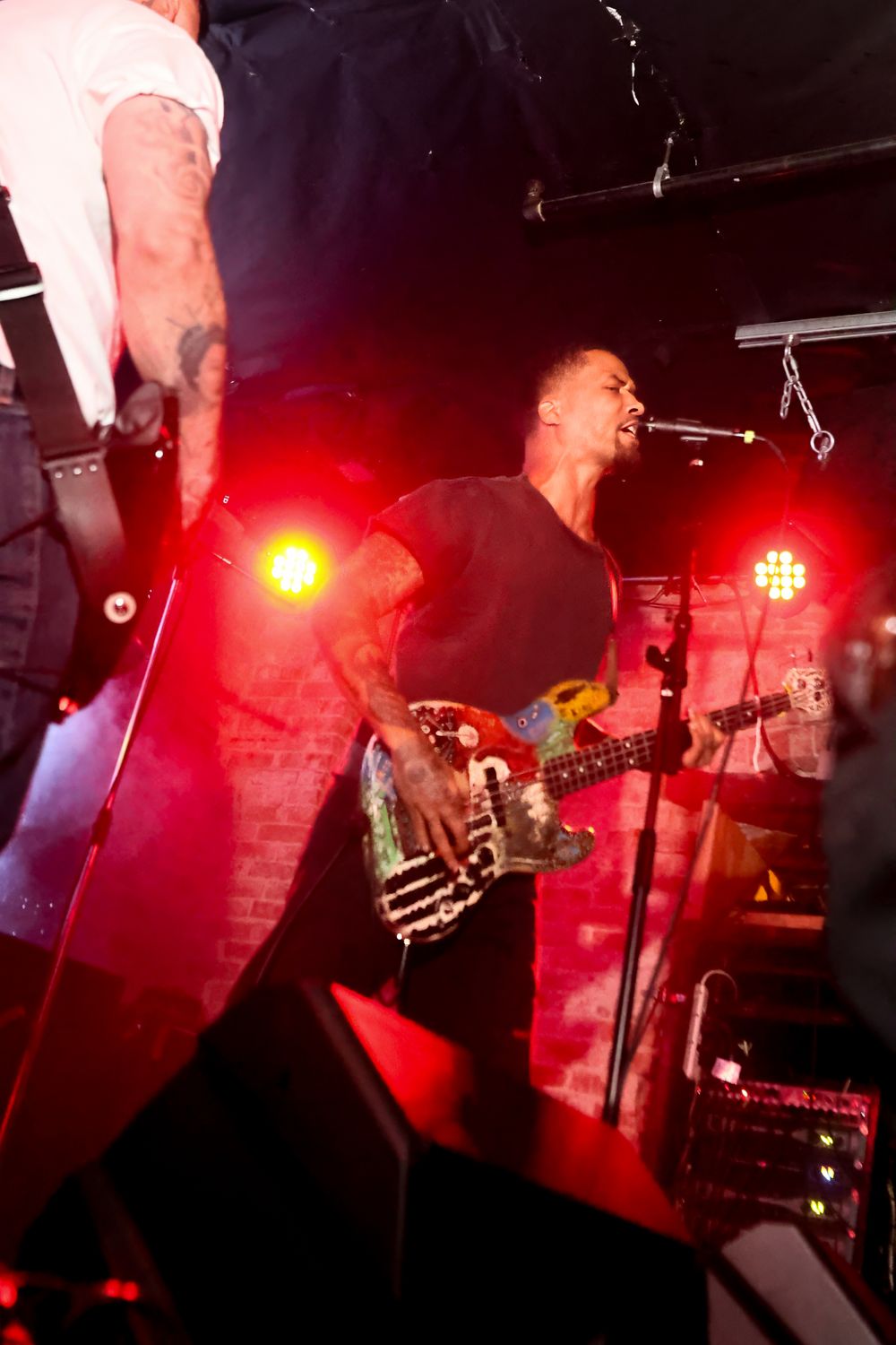 A rock band performs on stage with dramatic red lighting and energetic musicians playing instruments at a live concert.