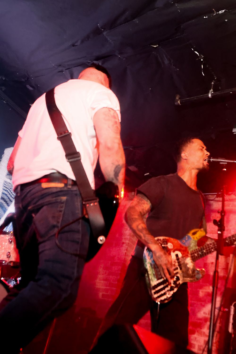 Musicians perform on stage under dramatic red lighting at a rock concert venue.