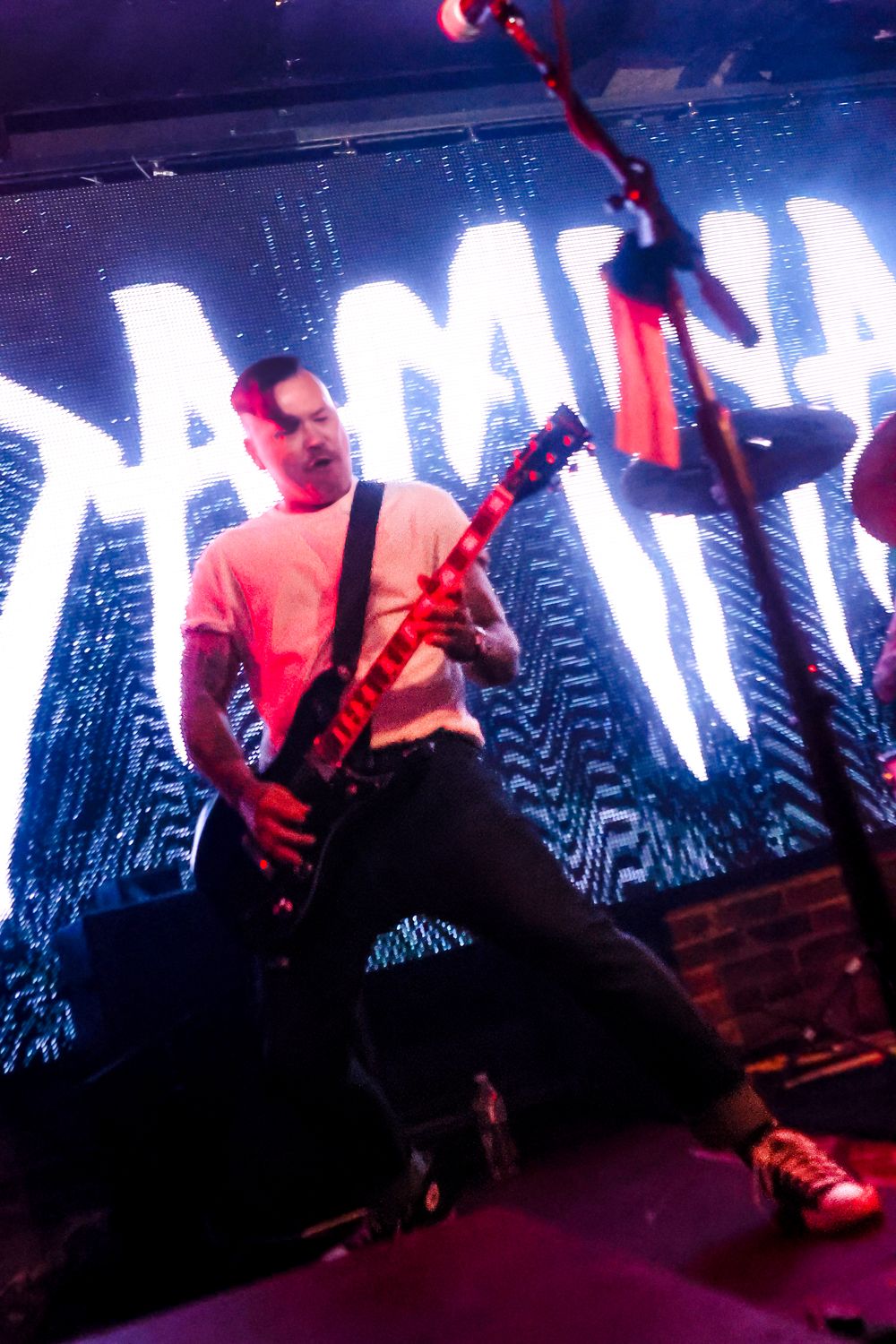 Musician performs energetically on stage with dramatic red and blue lighting effects during a live concert performance.