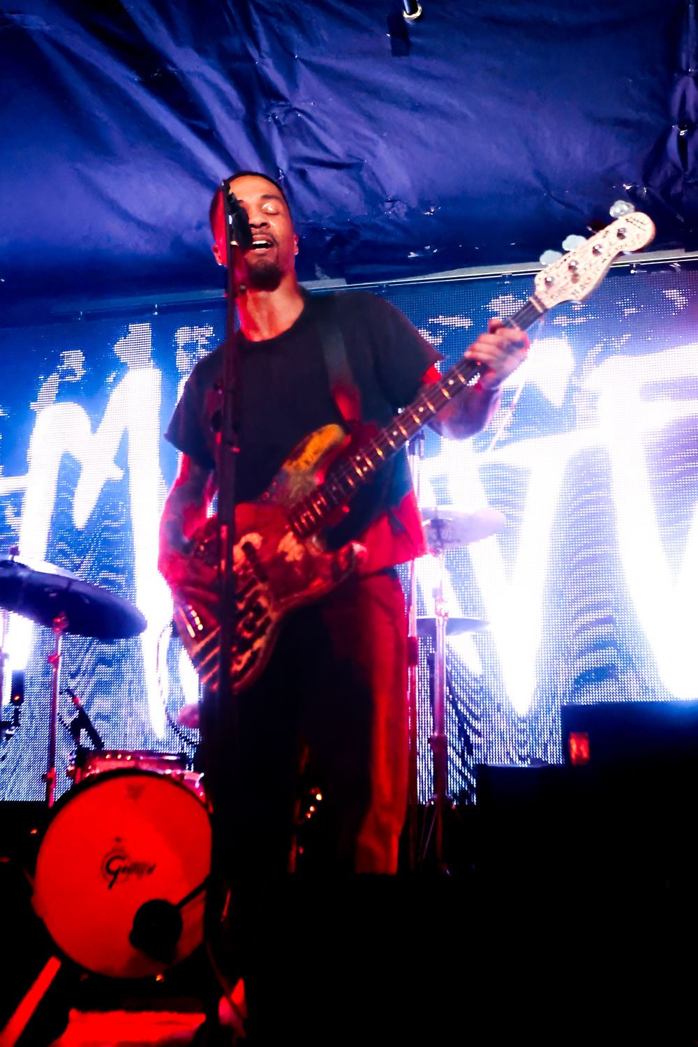 Musician performs on stage with electric guitar against dramatic blue and red lighting during live concert performance.
