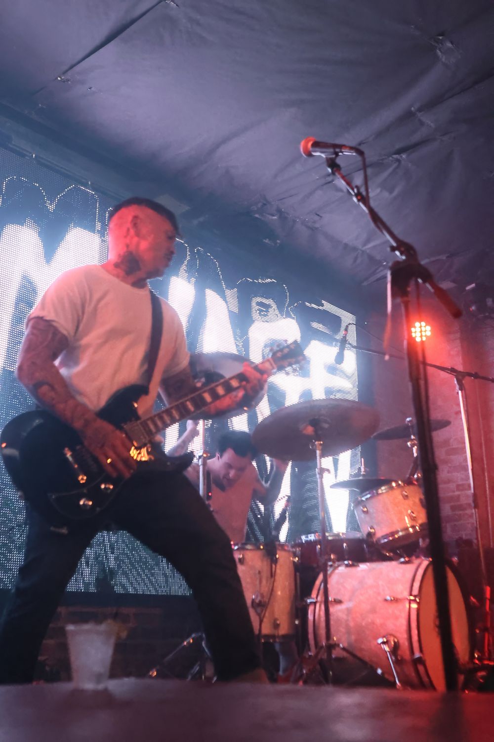 Musicians perform energetically on a dimly lit stage with dramatic red lighting and fog effects during a live concert.