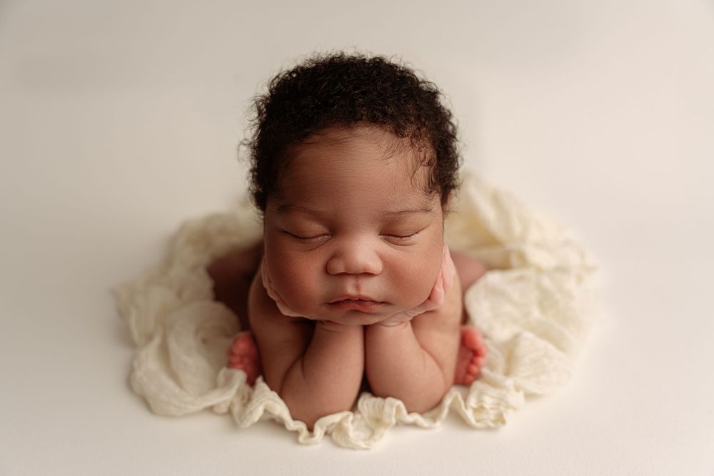 Peaceful newborn baby sleeping with chin resting on hands, posed on cream fabric, professional newborn photography.