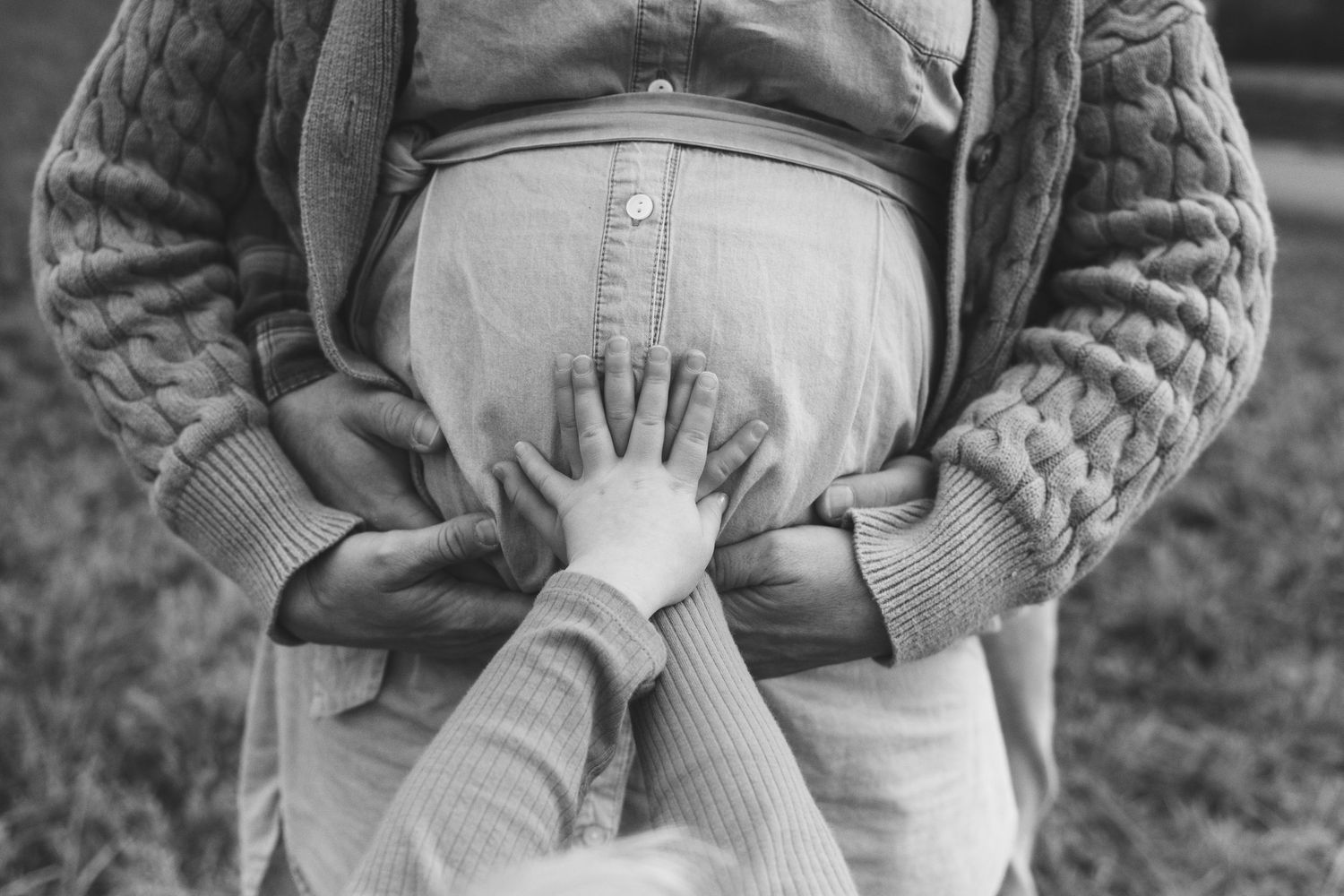 Black and white photo of small child's hands touching an adult's stomach in an intimate family moment.