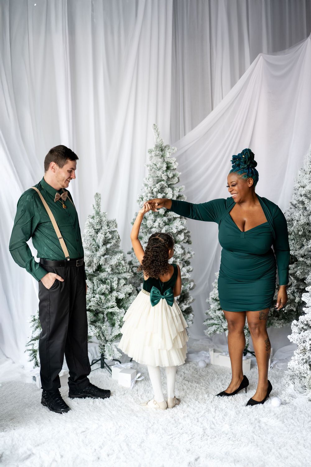 A mother in green dress twirls her daughter while father watches during a festive Christmas photo session.