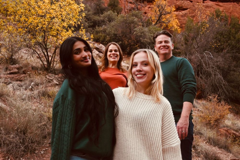 Two young women smiling in foreground with two friends behind them amid red canyon autumn scenery.