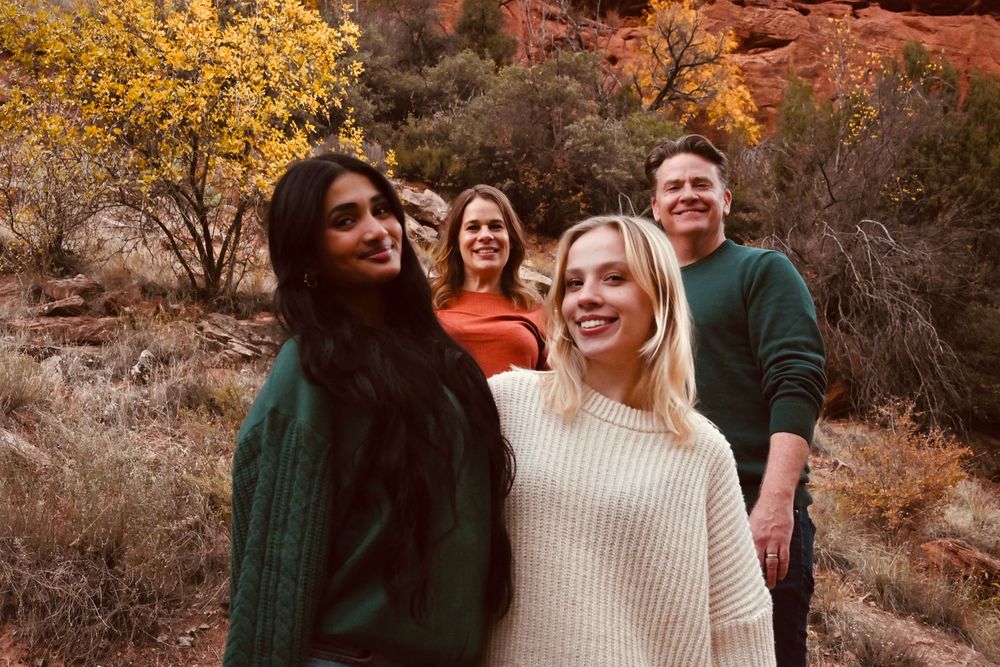 Group of five friends smiling together among red rock canyon scenery with autumn foliage in background.