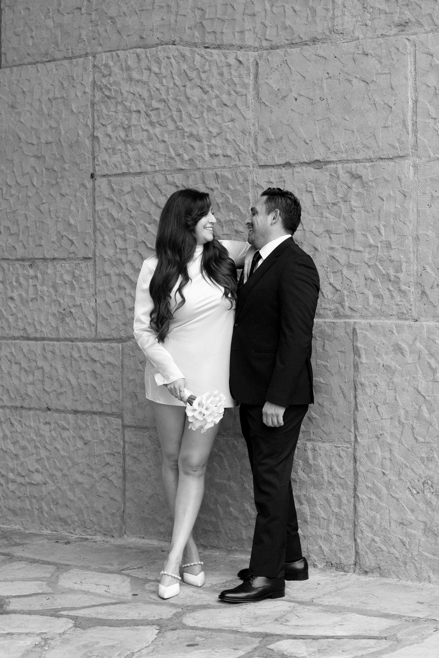 A series of black and white photos showing a playful romantic moment against a textured stone wall.