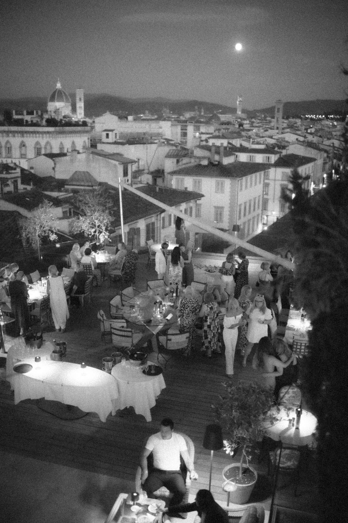 A black and white panoramic series of nighttime rooftop dining scenes in a Mediterranean coastal town.