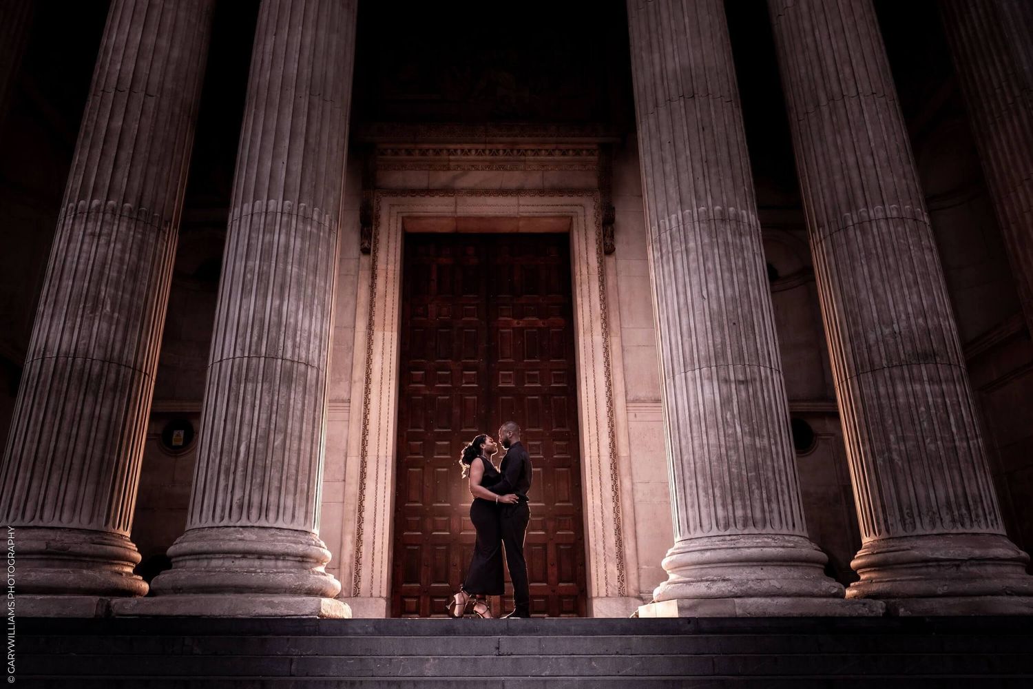 Illuminated neoclassical columns at night create dramatic shadows and perspective at a historic building entrance.