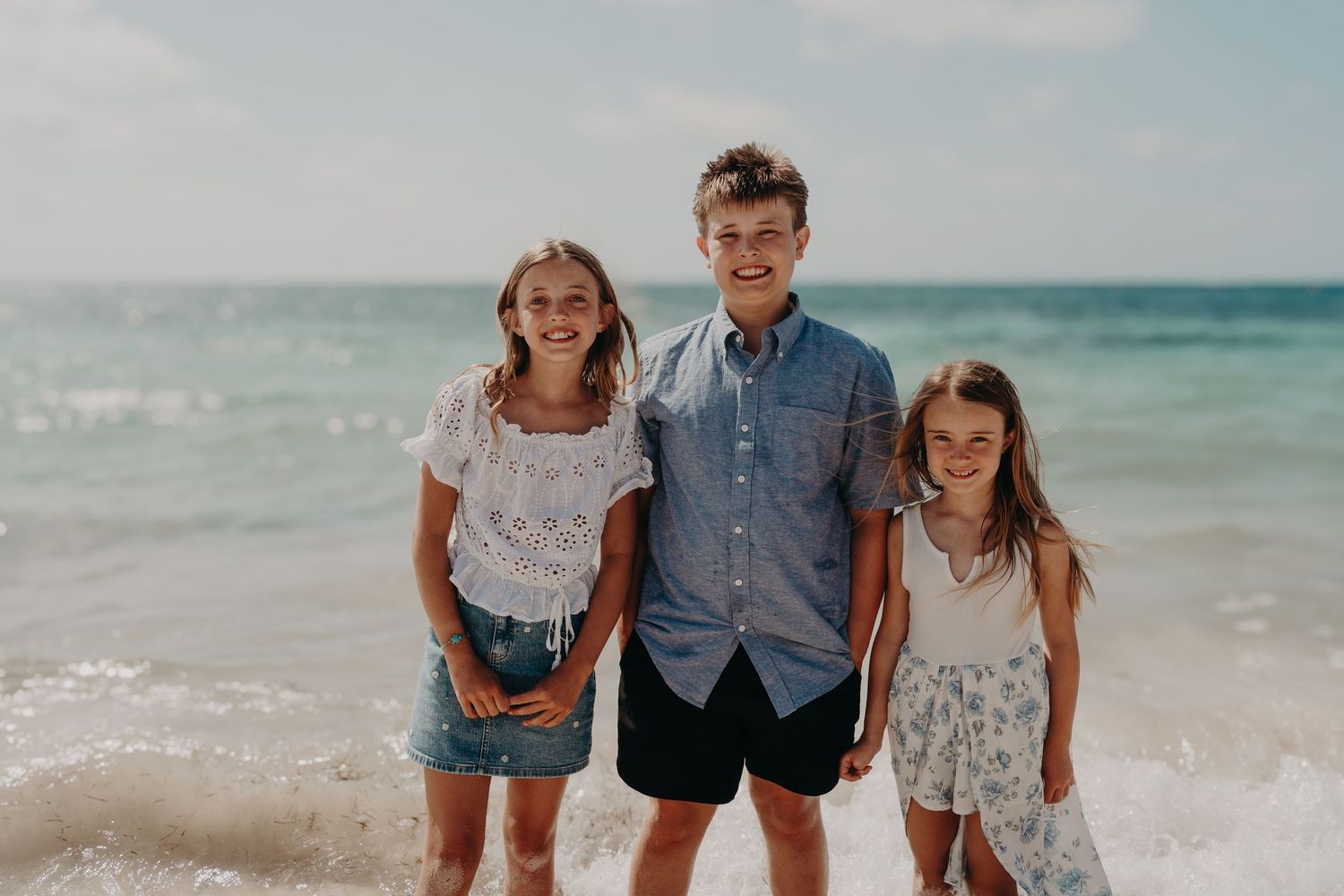 Family walking together along a beach shoreline with turquoise ocean waves and white sand in the background. Photography Puerto Morelos.