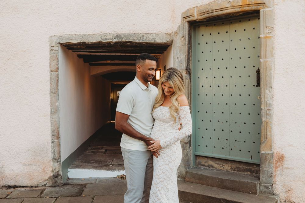 A couple shares an intimate moment together in front of a rustic mint green door and stone archway.