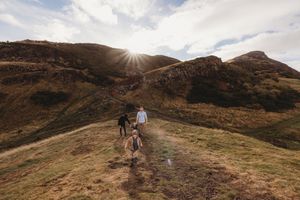 Hikers traverse scenic mountain trails at sunset with dramatic cloudy skies and golden light illuminating rugged terrain.