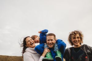 A joyful family laughs together outdoors against an overcast sky during a candid moment.
