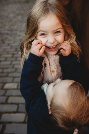 A playful sequence of candid moments showing two children laughing and interacting with pure joy on a cobblestone path.