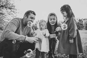 Black and white photo of a family blowing bubbles together outdoors in a park setting.