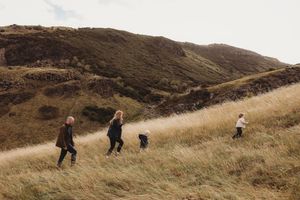 Hikers traverse a steep grassy hillside trail on a cloudy autumn day in the mountains.