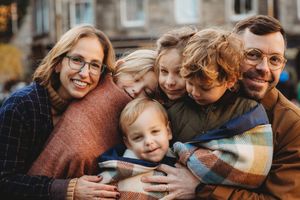 A close-knit family cuddles together outdoors on an autumn day wearing cozy sweaters and sharing warm smiles.