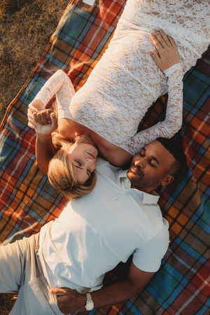 A couple lying together on a plaid blanket in warm sunlight during a romantic outdoor moment.