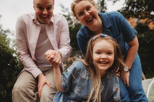 Two women and a young girl laughing and playing outdoors in a garden, capturing a joyful family moment.