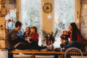 Family gathered by a festive window, sharing warm holiday moments in a cozy decorated living room.