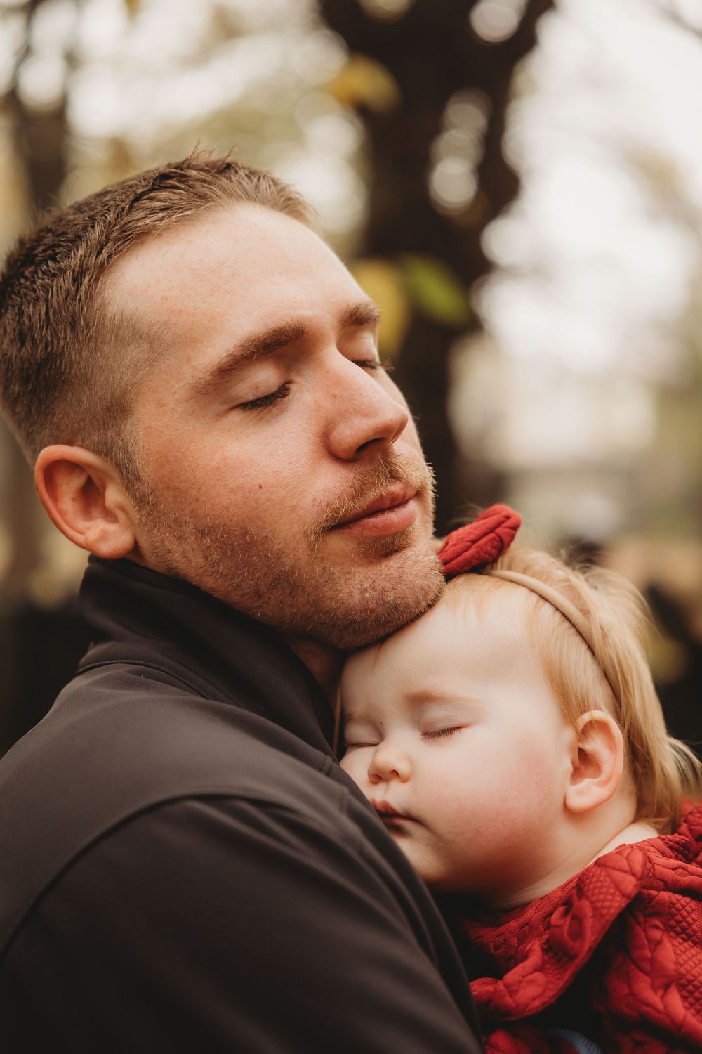 A parent in black jacket shares tender moments with a child wearing red in a series of intimate outdoor portraits.
