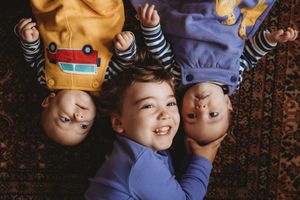 Three happy children lying on a rug, smiling and laughing together in colorful casual outfits.