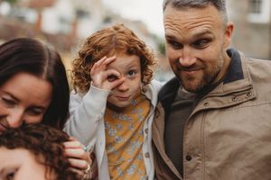 A cheerful redhead child makes an OK gesture with fingers while posing with smiling adults outdoors.