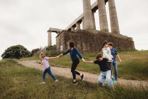 Children playing and running along a path near ancient stone columns monument on a grassy hill.