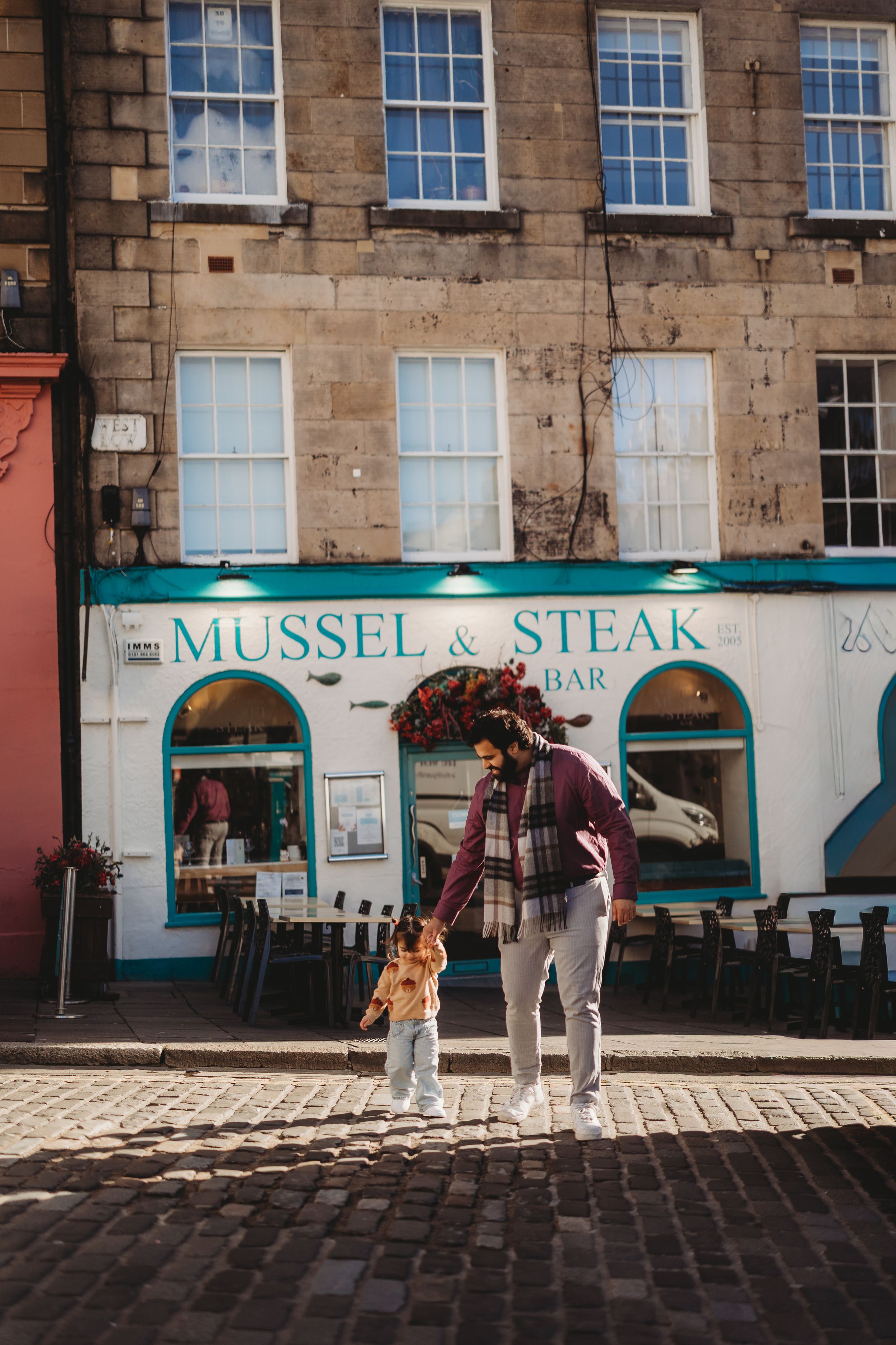 A person and child stand on cobblestones outside Mussel & Steak Bar in Edinburgh, Scotland.