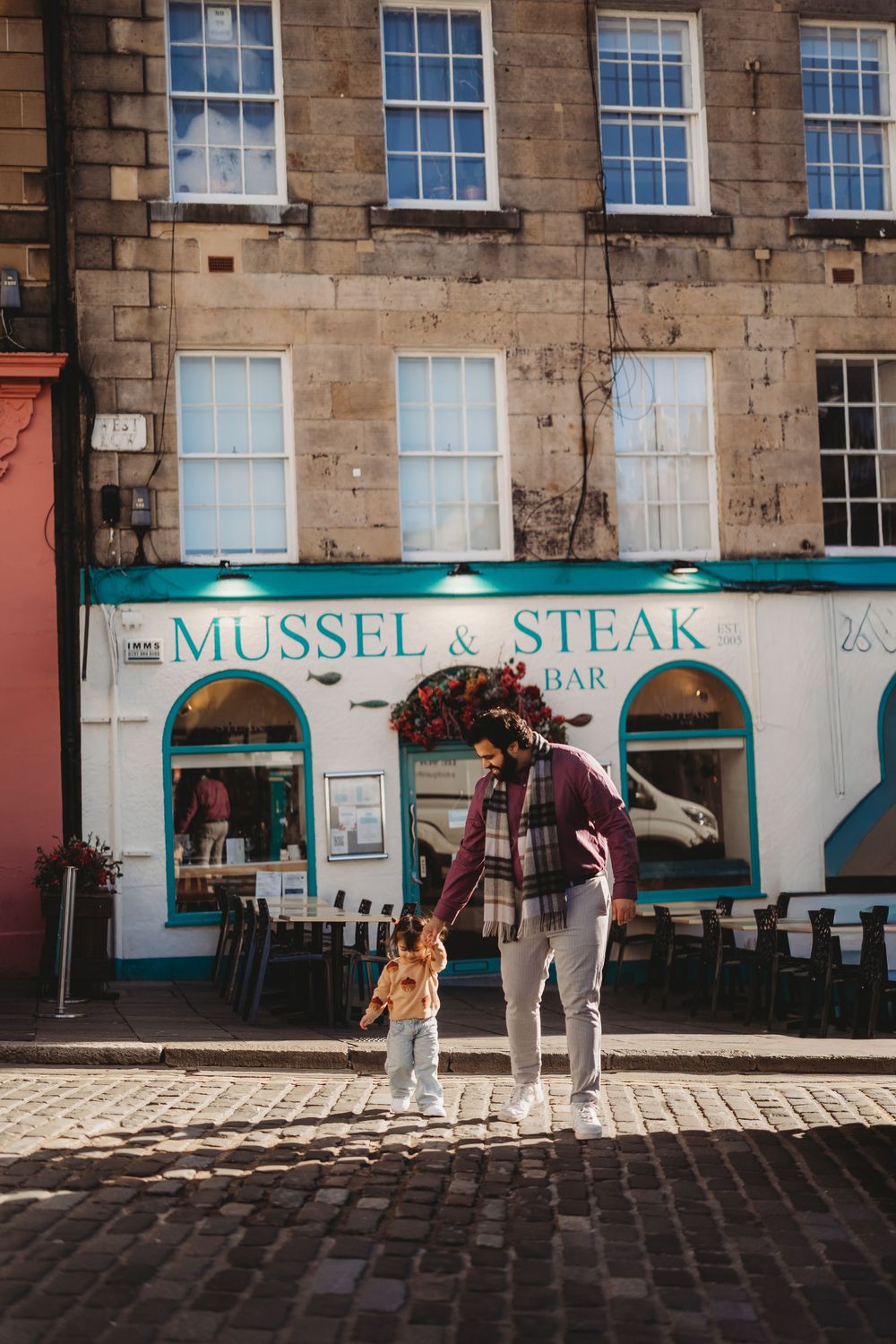 A person and child stand on cobblestones outside Mussel & Steak Bar in Edinburgh, Scotland.