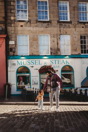 A person and child stand on cobblestones outside Mussel & Steak Bar in Edinburgh, Scotland.