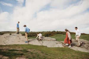 Group of people exploring cracked granite rock formation on a scenic hilltop under a cloudy sky.