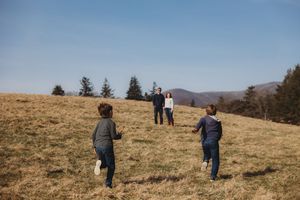 Two children running toward parents on a grassy hillside under a clear blue sky with mountains in the background.