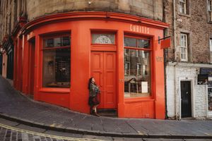 Bright red painted storefronts and brick buildings line a historic street corner in Edinburgh's Old Town.