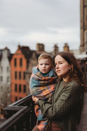Parent and child in warm winter clothing look out over city buildings on an overcast day.