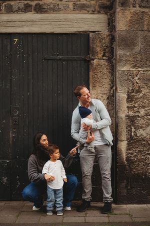 A series of candid family moments captured against a rustic stone wall with dark wooden doors.