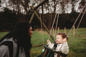 A mother smiles at her happy baby sitting in a garden swing outdoors.