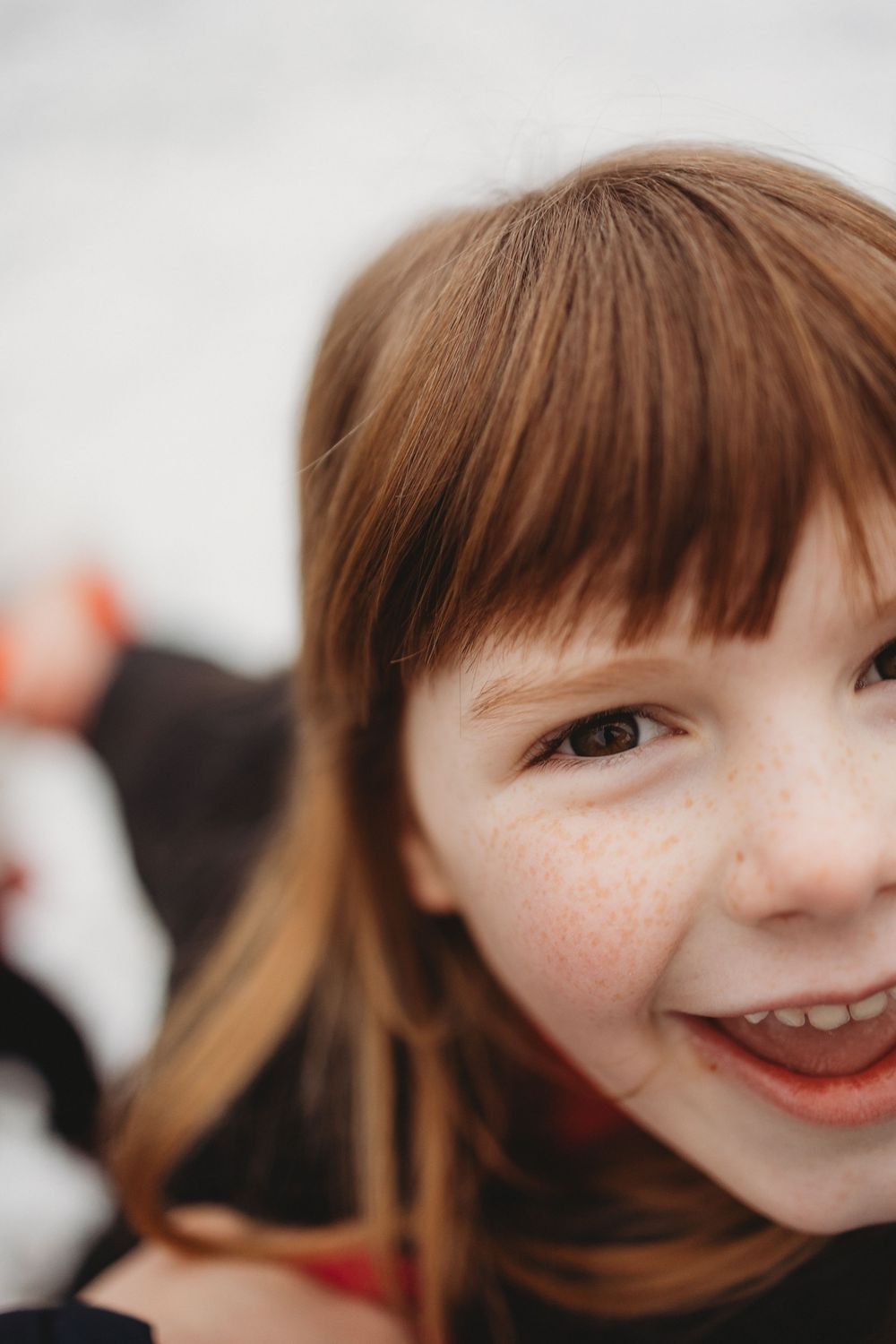 A smiling young girl with red hair, bangs, and freckles looks up at the camera with a cheerful expression.