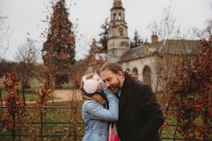 A father and daughter share a tender moment in an autumn garden with a historic church in the background.