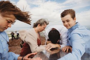 Group of young people gathered around a table outdoors on a windy day with cloudy skies in the background.