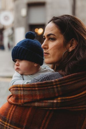 A couple shares a cozy moment wrapped in a warm plaid blanket while looking off into the distance on a winter day.