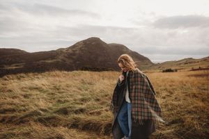 A couple walks through a scenic mountain landscape with brown grass and moody overcast skies.