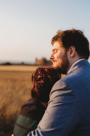 A couple embraces in a golden wheat field at sunset, with warm light illuminating their silhouettes.