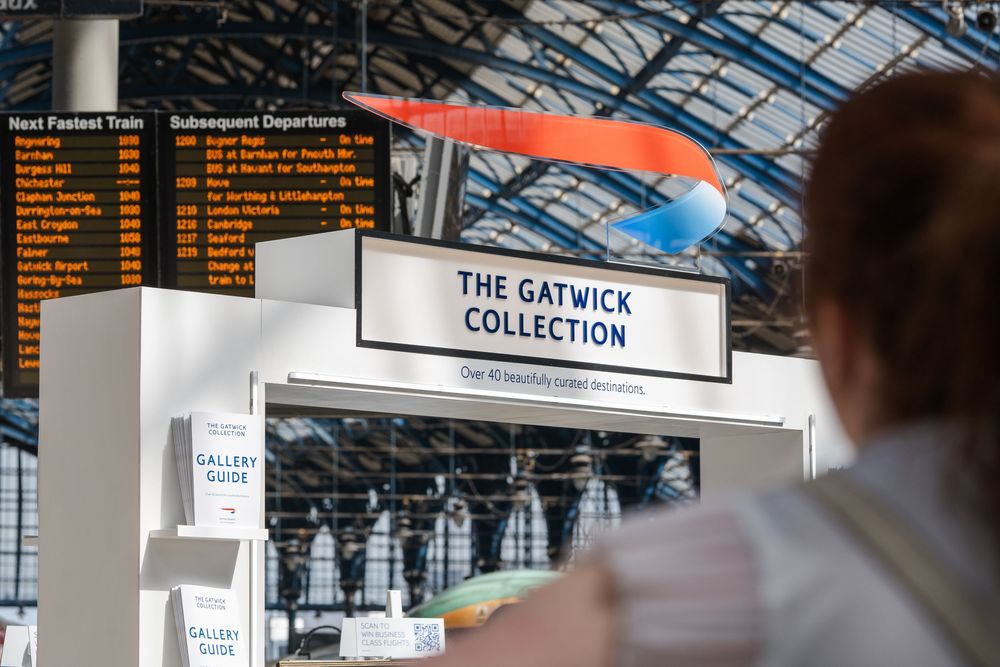 Interior view of a train station or airport terminal with 'The Gatwick Collection' signage visible.