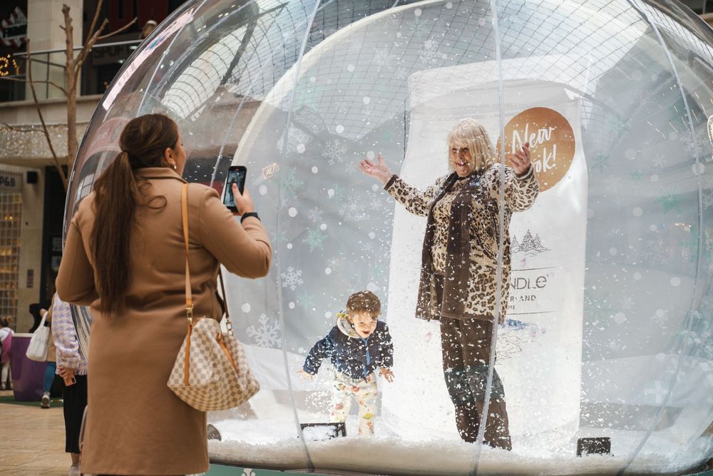 Large transparent snow globes displayed in a shopping area with people visible inside.