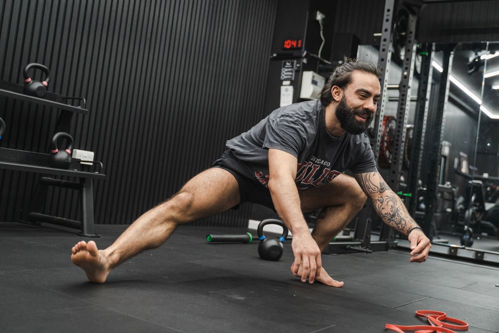 Fitness enthusiast stretching on gym floor with red exercise equipment.