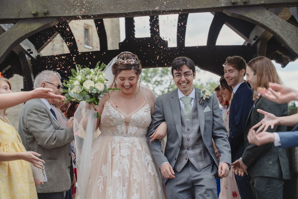Wedding celebration with guests throwing confetti under a rustic stone archway.