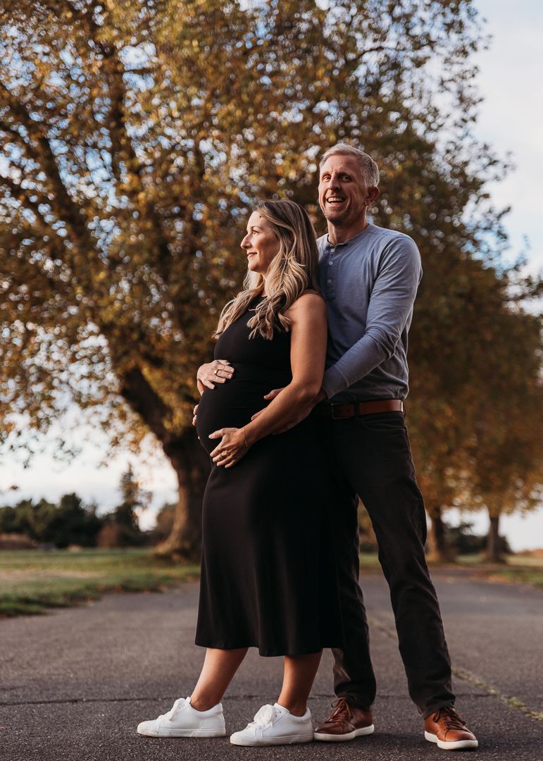 A couple in casual attire sits together on steps during a warm autumn day with golden trees in the background.