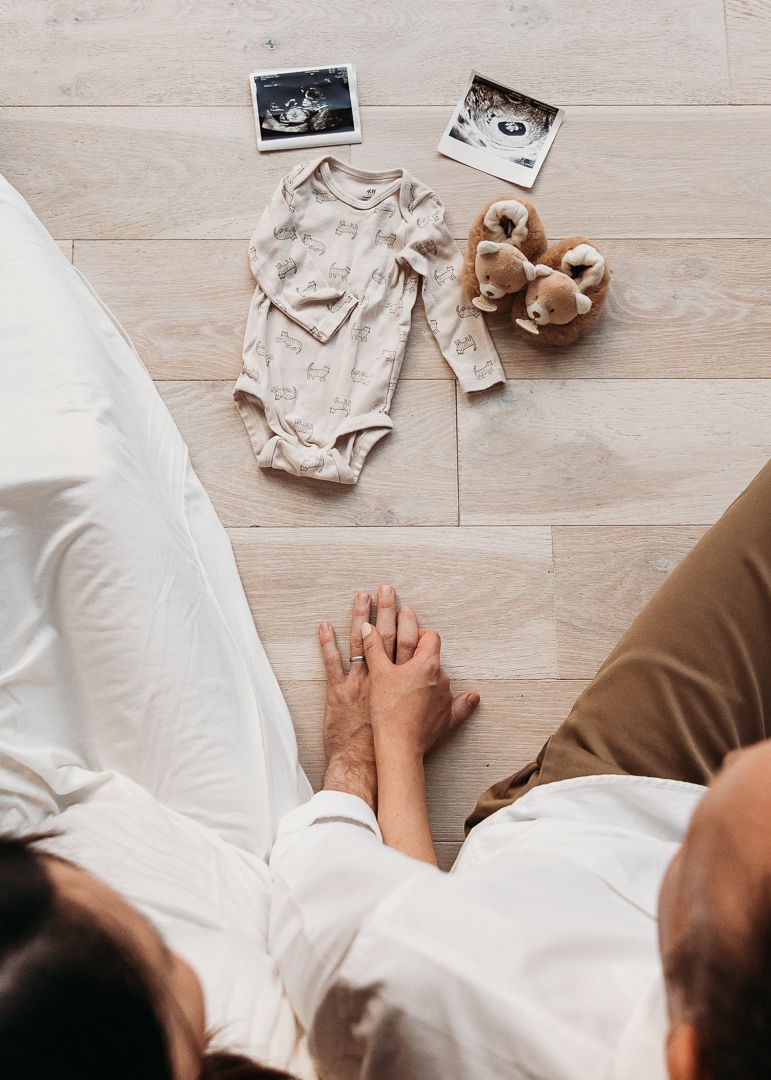 A series of ultrasound photos laid out on a wooden floor next to baby clothes and stuffed animals.