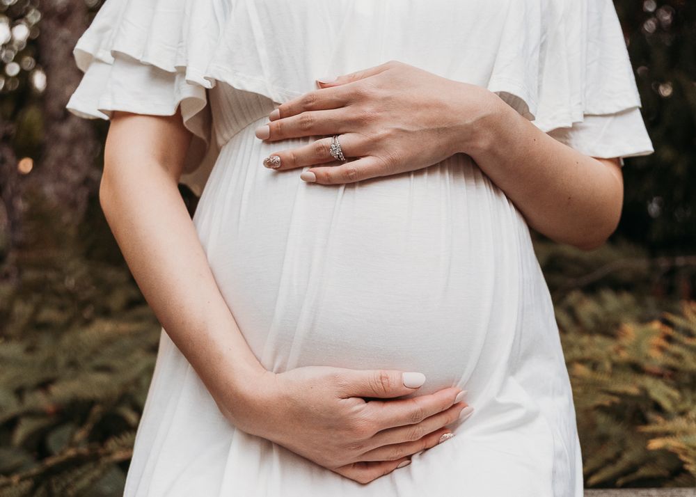 A series of maternity photos showing hands cradling a pregnant belly in a white dress against a dark background.